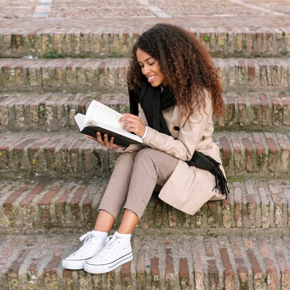 Woman sitting on outdoor steps reading a book, representing continuing education for clinicians